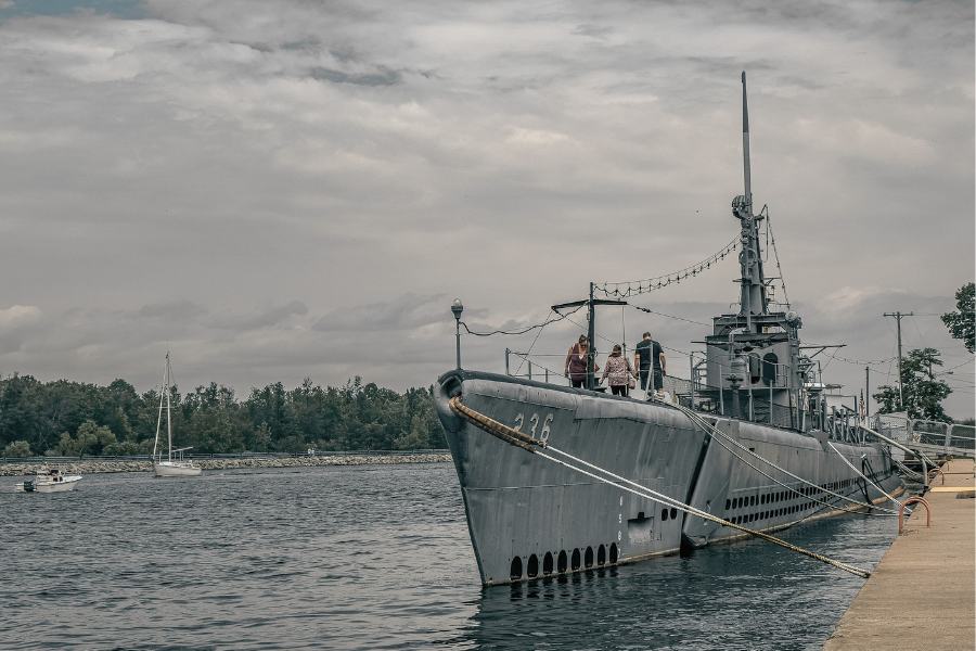 Visitors aboard the USS Silversides, a World War II submarine, docked at Muskegon Channel under a cloudy sky.