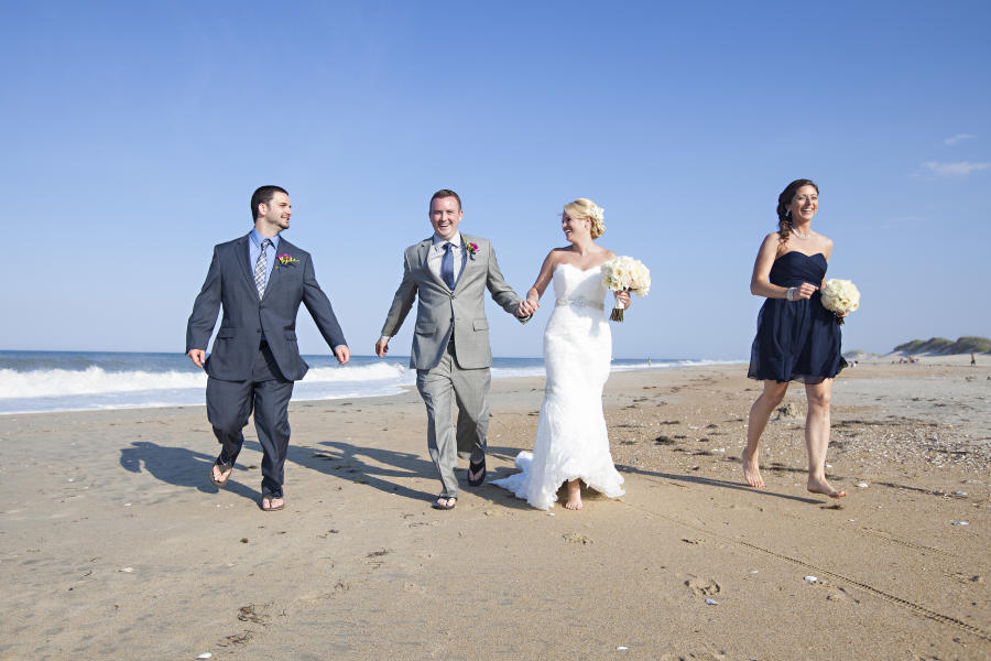 Bride & Groom With Wedding Goers Running On A Beach On The Outer Banks Of NC