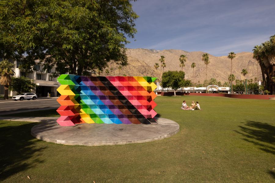 Palm Springs Pride Monument with two people sitting next to it on the lawn.