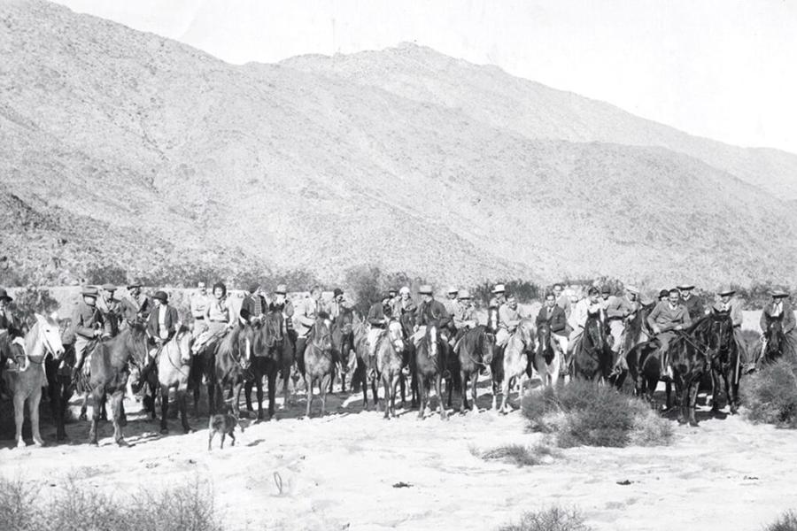Vintage black‑and‑white photo of riders on horseback gathered at the opening of the Lykken Trail in Palm Springs, set against rugged desert mountains.