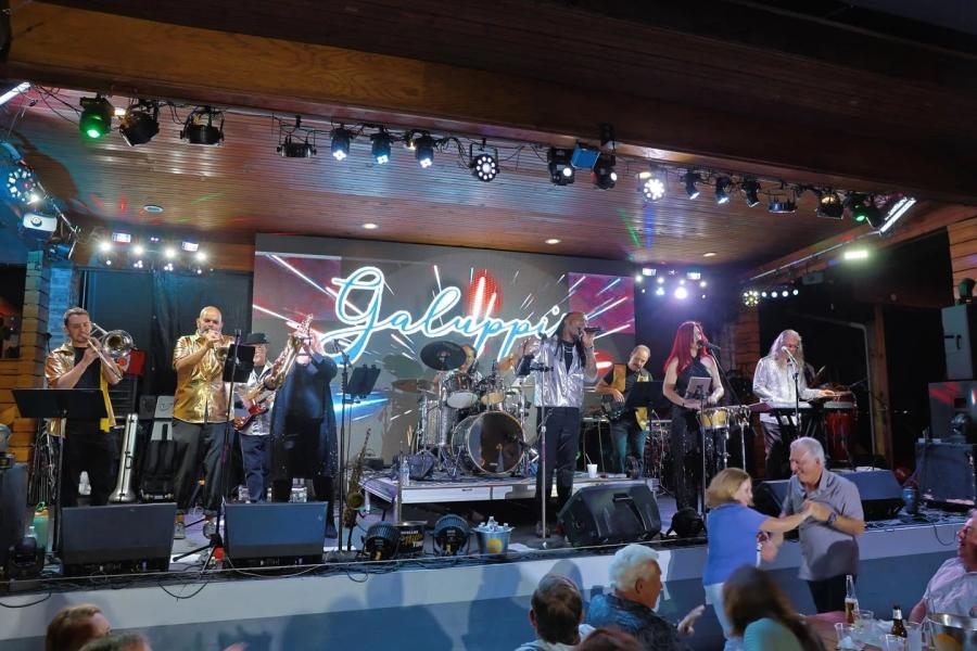 A band with nine members playing on Galuppi's Mainstage in Pompano Beach, in front of a crowd A couple dance is dancing in front of the stage