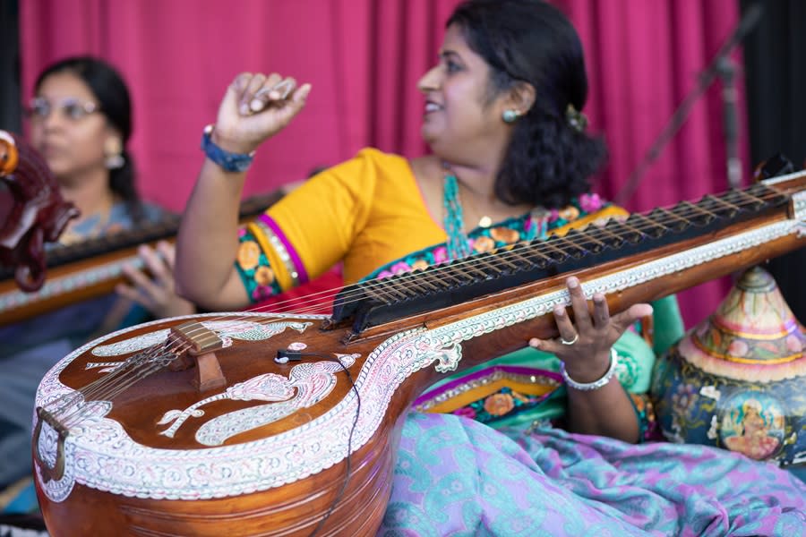 A young lady dressed in traditional Indian clothing sitting on the floor of a stage playing a sitar at the Namaste! Festival in Pompano Beach, FL.