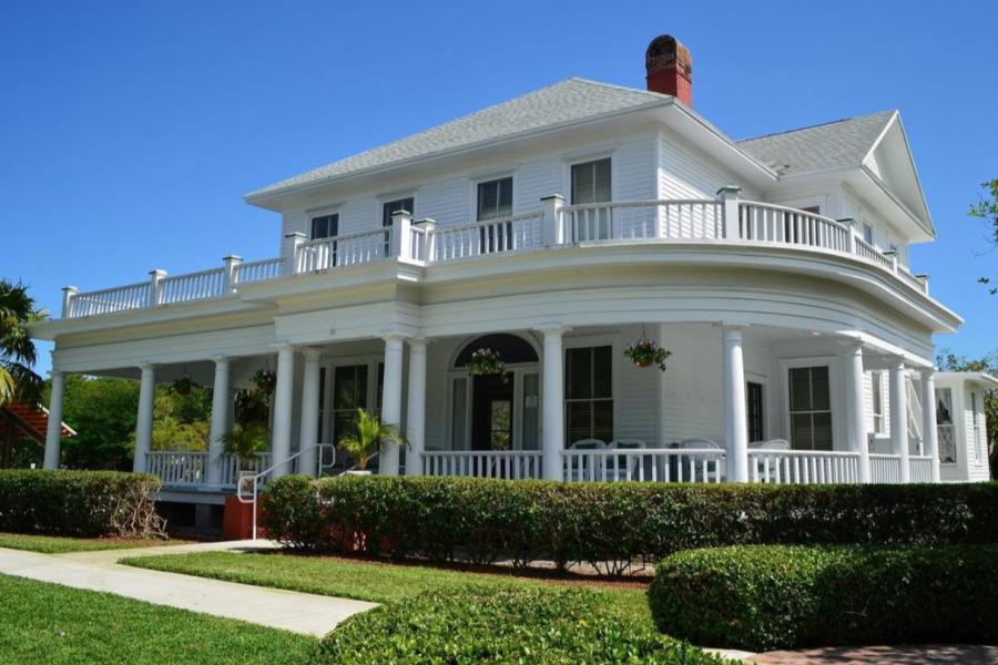 A large white house with a fenced-in covered porch and beautifully landscaped bushes, grass, and a walkway in Pompano Beach
