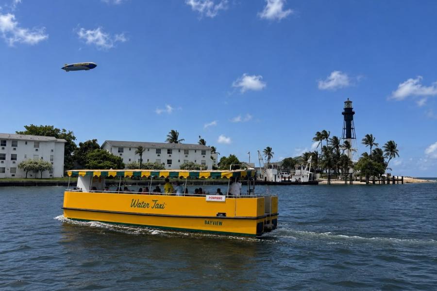 The Pompano Beach Water Taxi in the Hillsboro Inlet, with the GoodYear Blimp in the sky and the Hillsboro Lighthouse in the background.