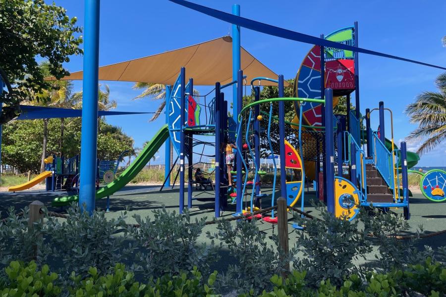 A kids' playground next to the beach, under two large sun shades.