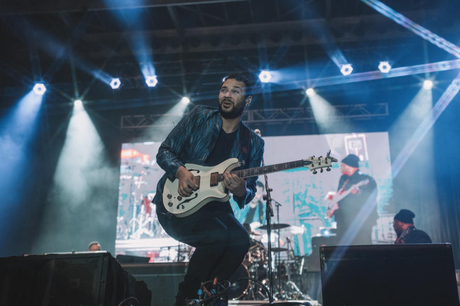 A performer on an outdoor stage at night, playing the electric guitar