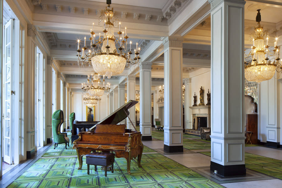 Hotel lobby with green carpeting, large chandeliers, and grand piano