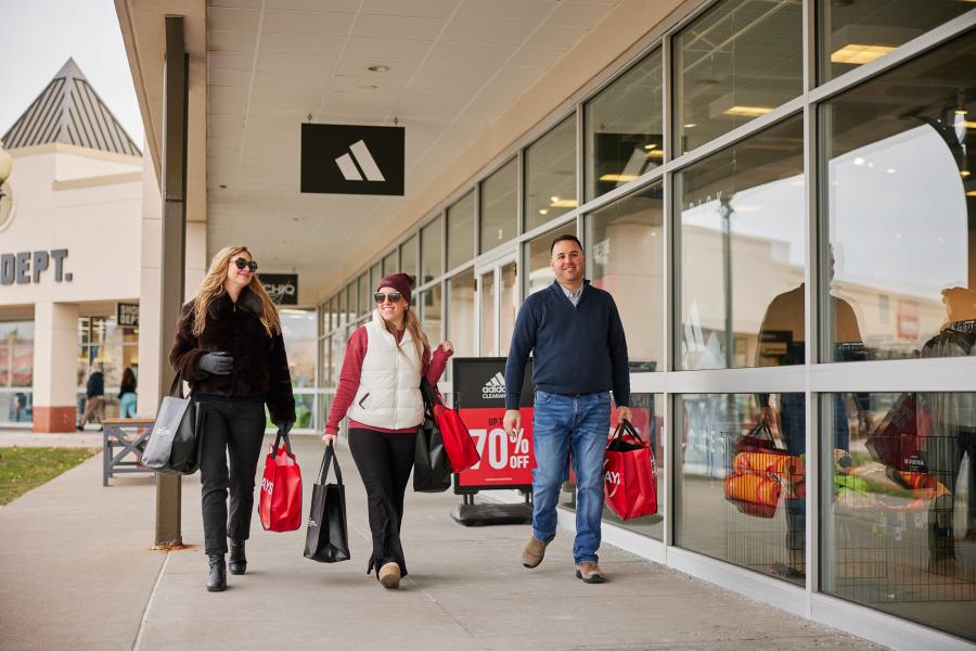 Three people walking at an outdoor mall holding shopping bags in winter