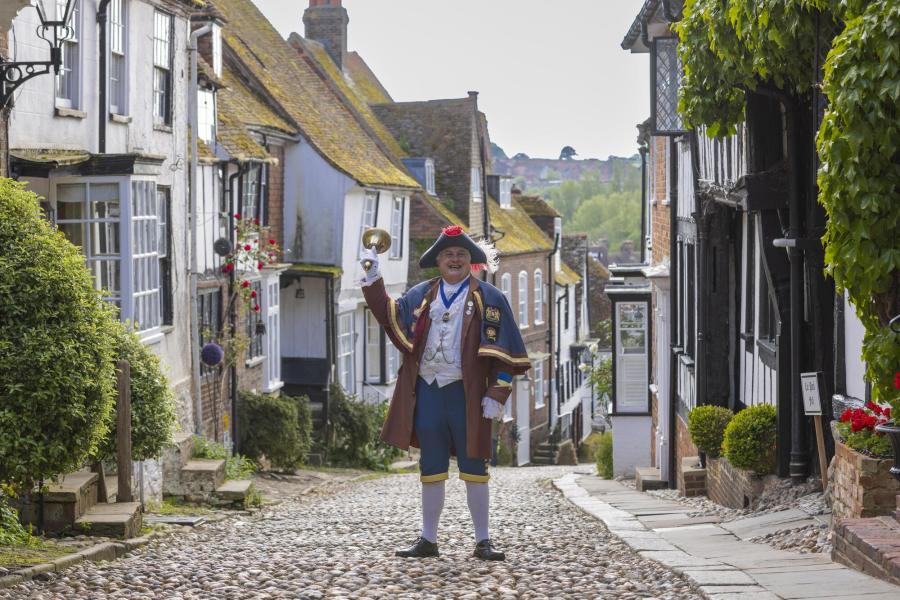 Rye cobbled street with Town Crier holding up his bell wearing traditional costume