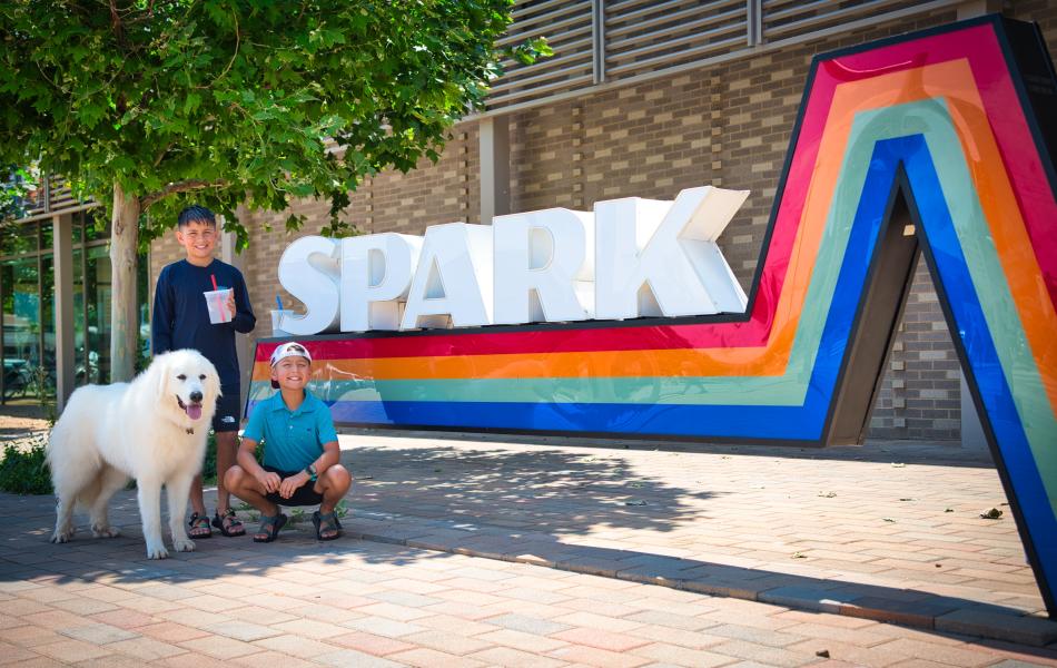 Two boys and a dog posing in front of Spark in Scissortail Park