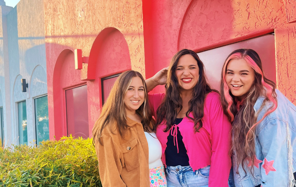 Three ladies smiling in front of a pink building