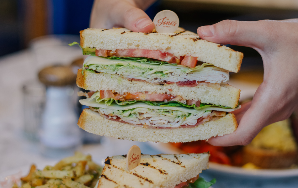 Set of hands holding a turkey club sandwich at Jones Assembly