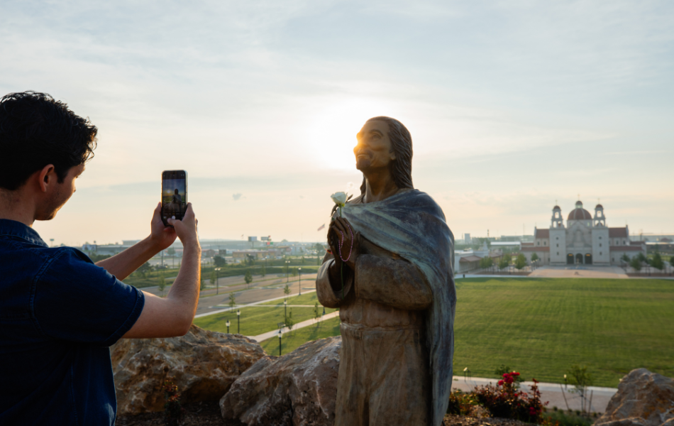 Man taking a photo of a statue with the Stanley Rother Shrine in the background