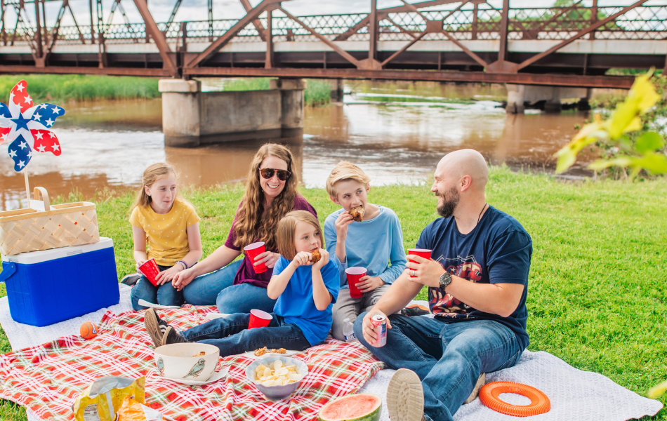 A family eating a picnic on a red and white blanket