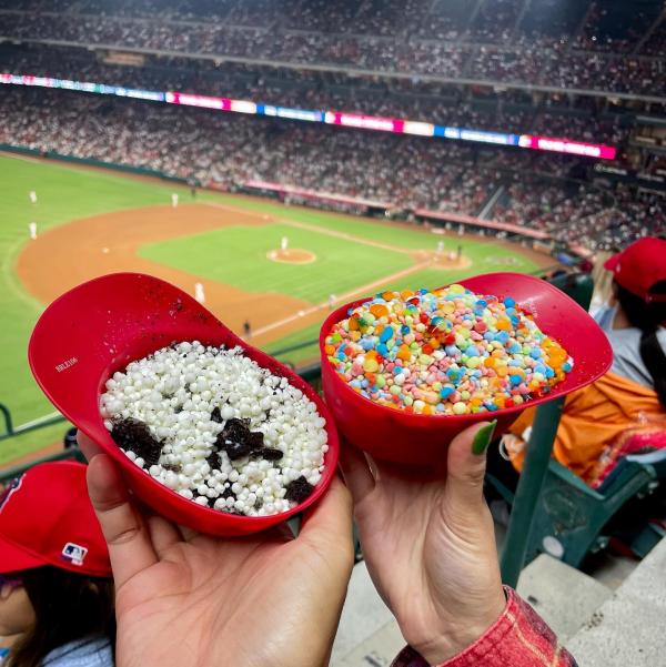 Image of two red helmets filled with dippin' dots ice cream being held in front of a green baseball field.