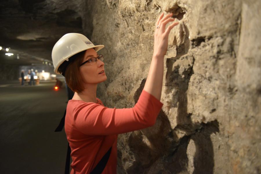 Woman in hard hat explores wall of cave