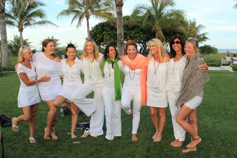 Nine ladies dressed in white lined up with their arms around each other on the Great Lawn in Pompano Beach, FL.