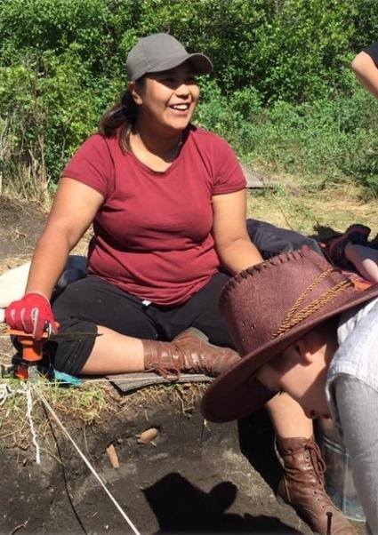 A woman sits on the ground at an archaeological dig site