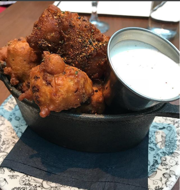 bowl of fried corn fritters with silver cup of sauce on a plate at coppins at hotel covington ky