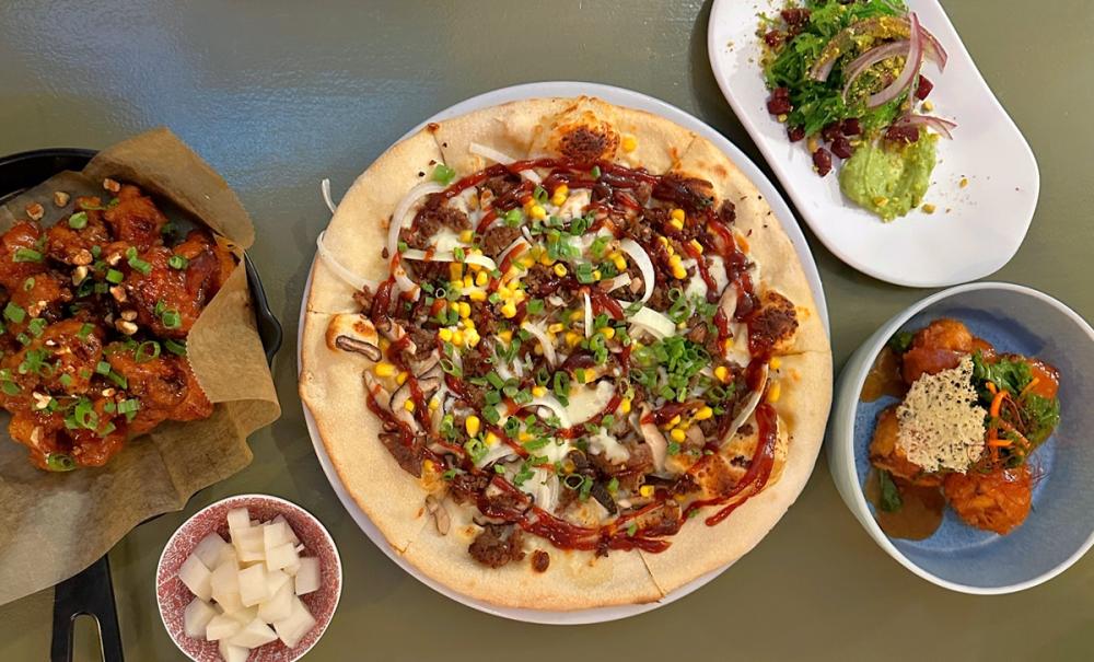Photo taken from directly above food, showing full pizza with drizzled toppings and various side dishes on plates.