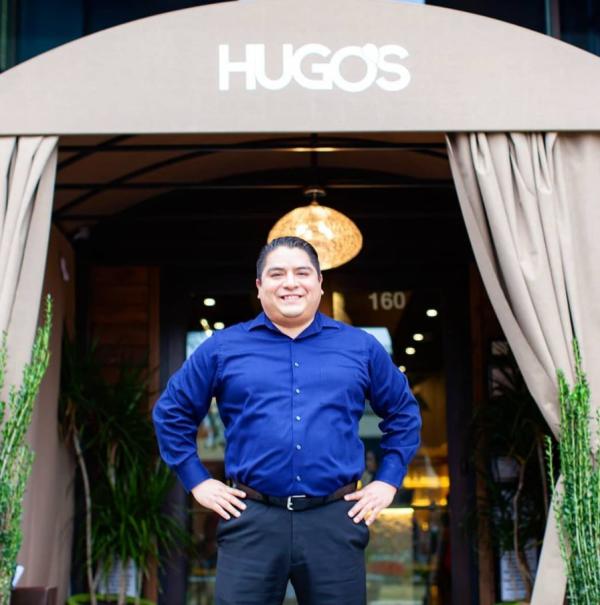 Restaurant owner, Hugo, standing proudly with his hands on his hips in front of the Hugo's restaurant