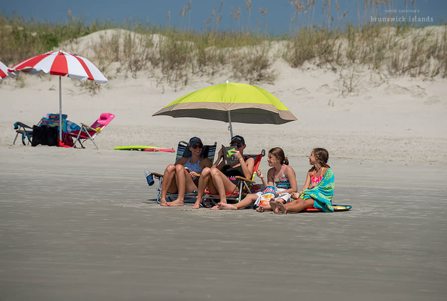 a family of 4 sitting on the beach under an umbrella
