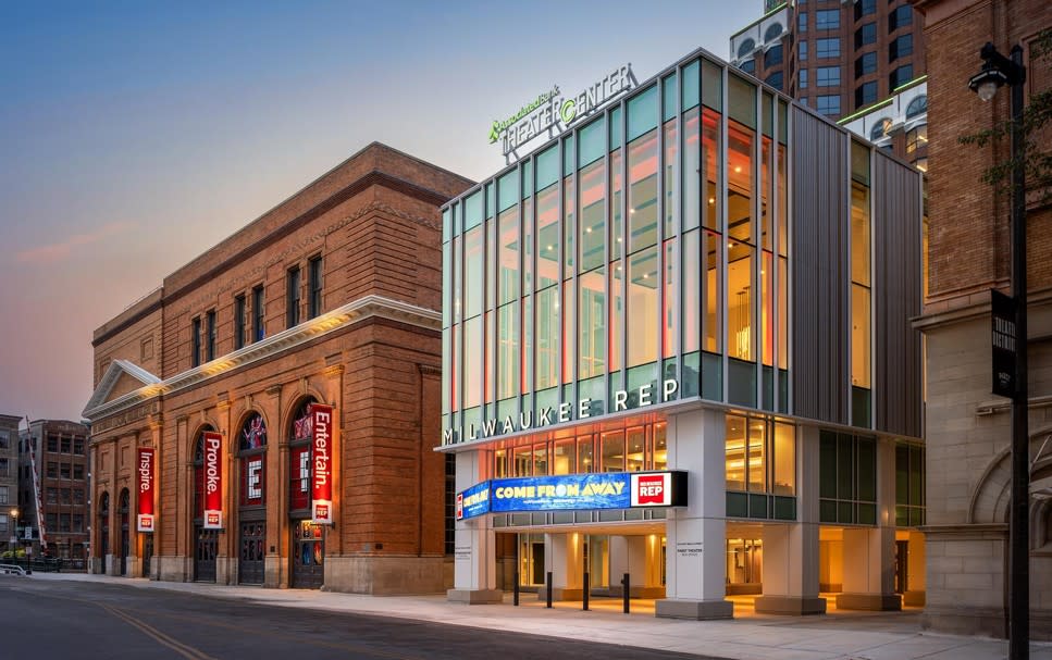 Associated Bank Theater Center in downtown Milwaukee, featuring the glass-front Milwaukee Repertory Theater entrance next to the historic brick theater building at dusk.