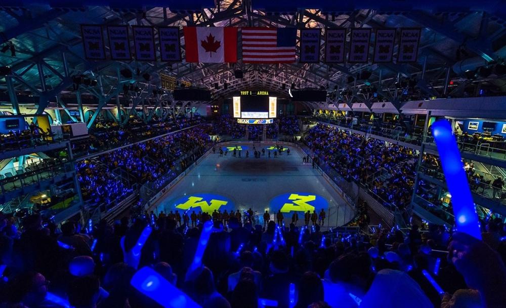 Dimly lit ice skating arena during a hockey game. The stands filled with cheerful fans.