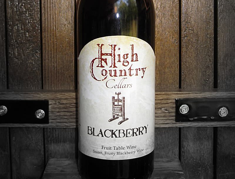 A bottle of wine in front of a wooden door with a label that reads "High Country Cellars Blackberry"