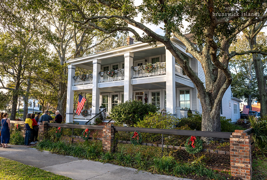 a group of people lined up outside to enter a house decorated for Christmas