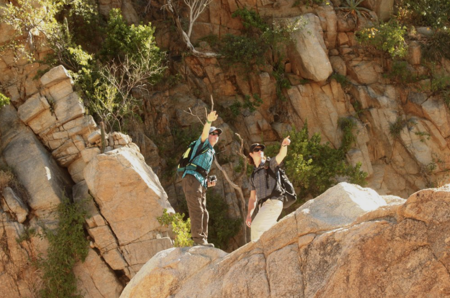 Two people on top of a rock waving at the camera