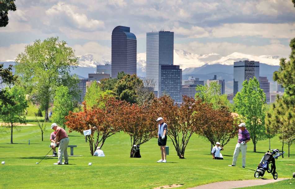 Golfers at City Park with Denver skyline and mountains.