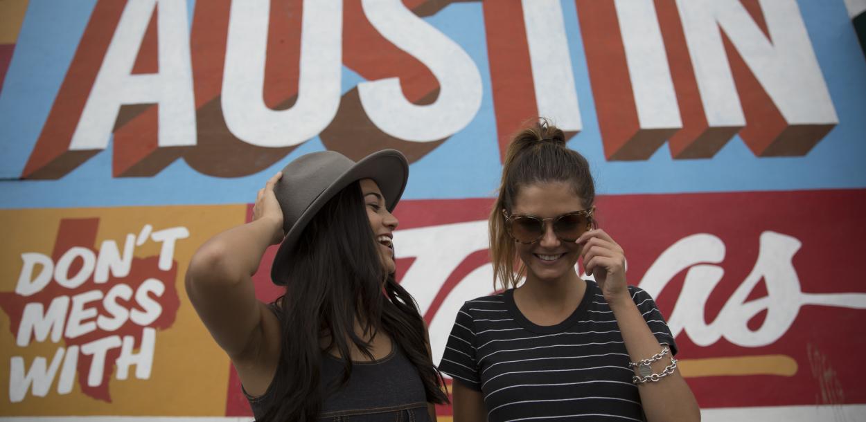Two girls laughing in front of Austin mural