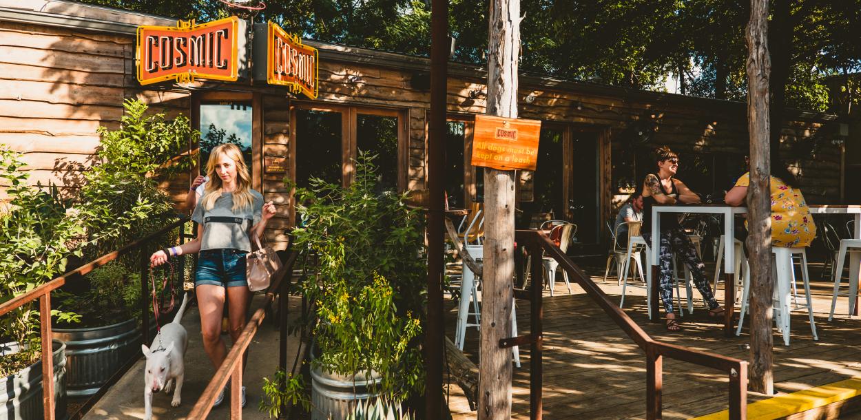 Woman walks down the ramp with a dog outside Cosmic Coffee and Beer Garden in Austin Texas