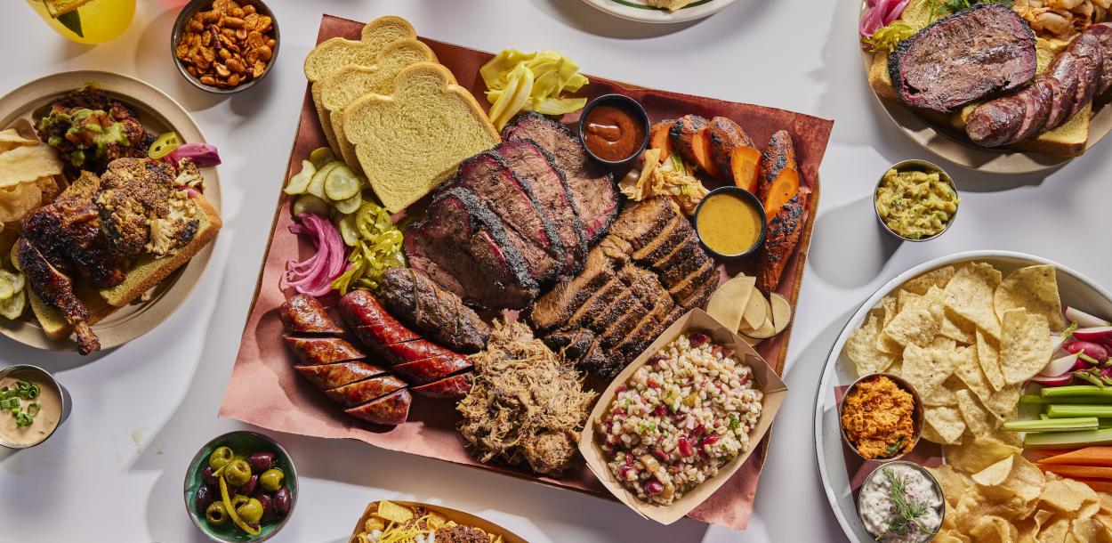 Colorful plates and trays of LeRoy and Lewis Barbecue, including sausage, brisket, frito chili pie, chips and crudite and more.