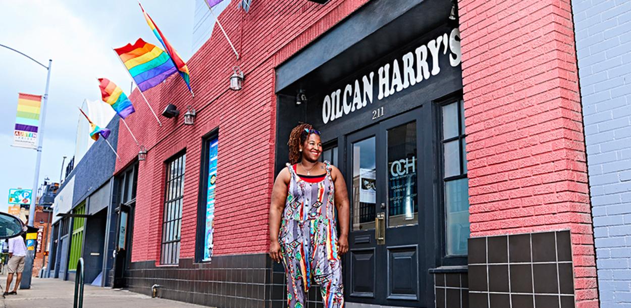 LaGina Harris stands on the sidewalk outside of Oilcan Harrys in the Warehouse District with rainbow flags on the building behind her