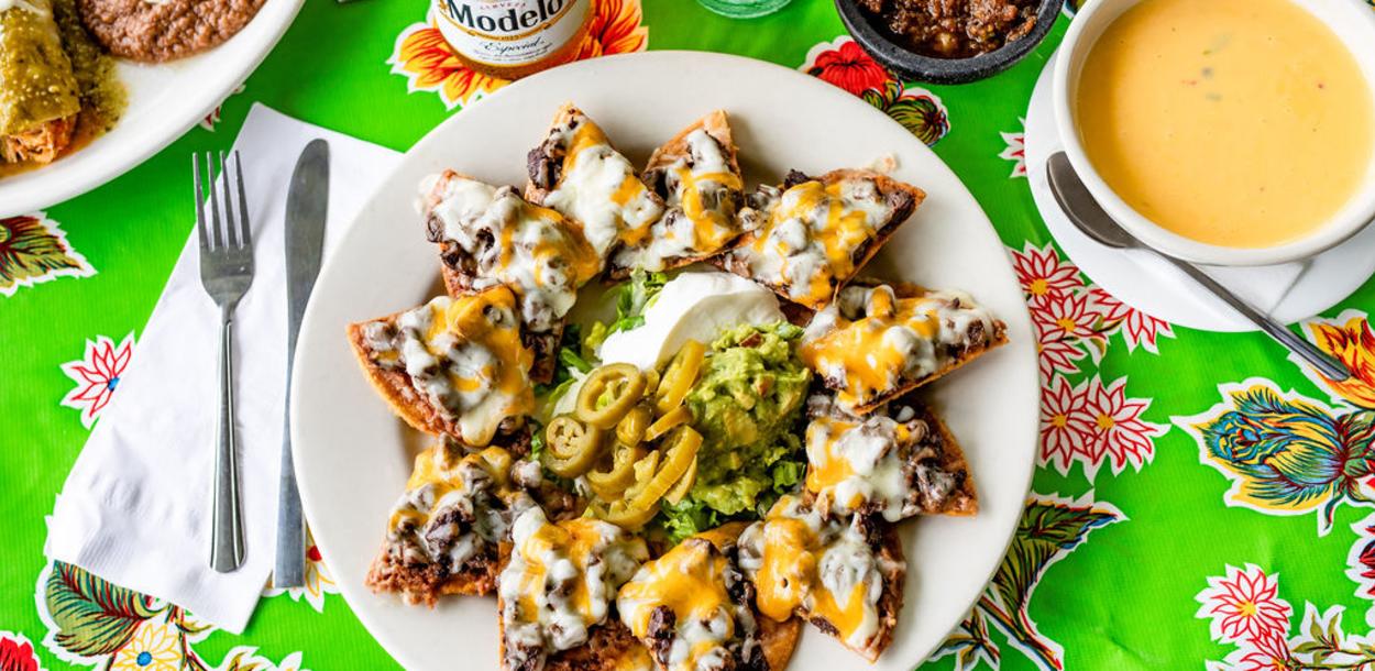 Mandito's Beef Nachos with sour cream, guacamole and jalapenos on a plate next to a bowl of queso, a modelo beer and a topo chico