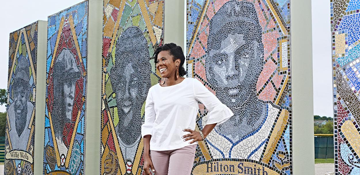 Nefertitti Jackmon stands in front of the mosaic of iconic Black baseball players at Downs Mabson Field in East Austin Texas