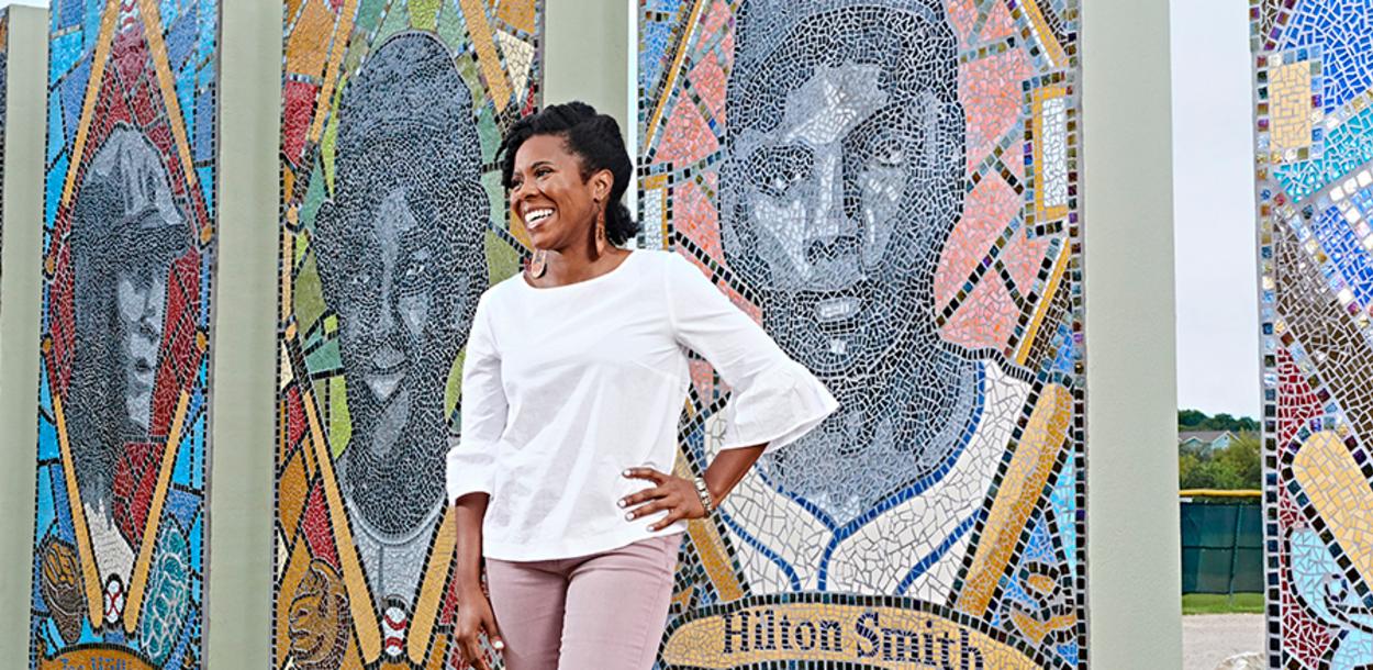 Nefertitti Jackmon stands in front of the mosaic of iconic Black baseball players at Downs Mabson Field in East Austin Texas