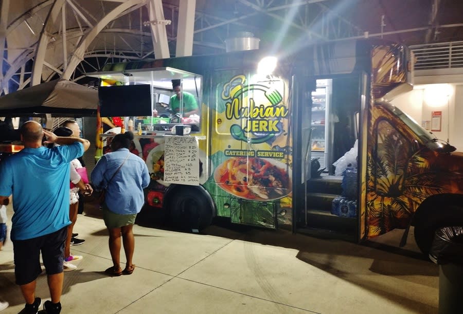 A food truck that says "Nubian Jerk Catering Services" on the side, parked and selling at an an evening event.