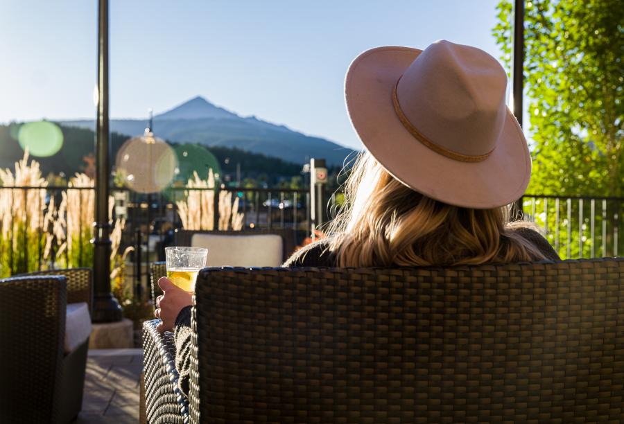 Person with hat enjoying a drink on a patio with a mountain in the background.