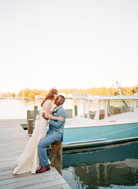 A bride and Groom stand by a blue boat on the water.
