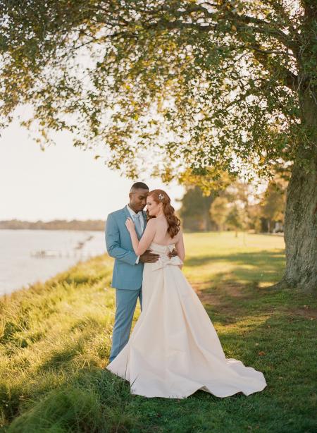 A wedding couple under a tree by the water.