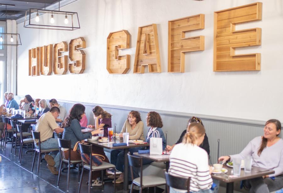 Hugs Cafe spelled out in wooden letters on wall with tables and customers beneath the sign