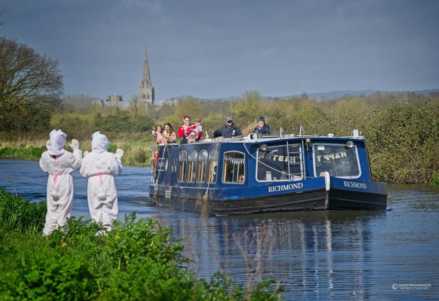 Easter bunnies wave at passengers on a Chichester Canal Easter boat trip with Chichester Cathedral in the background