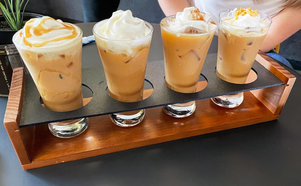 Four small drinking glasses filled with coffee and topped with whipped cream