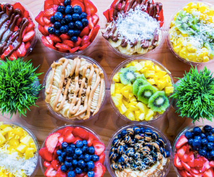 Many bowls filled with different kinds of colorful fruit and smoothies