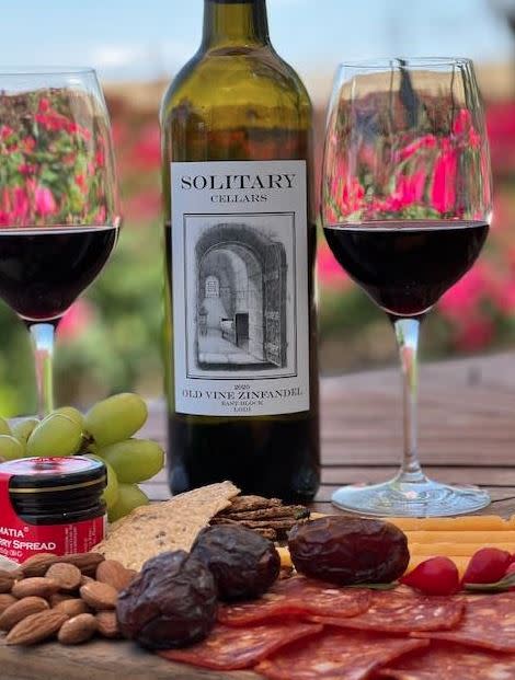 Two glasses of red wine with tray of meats, fruits and cheese