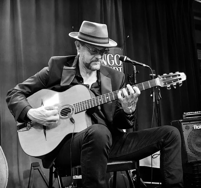 Michael Joseph Harris plays a guitar on stage (man in a black and white photo with a beard and wearing a hat)