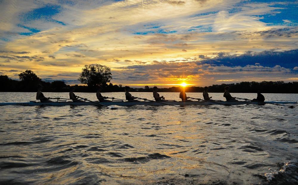 9 people rowing boat on a lake during sunset